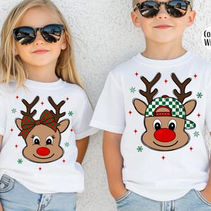May include: White t-shirts with reindeer graphics. One shirt features a reindeer with a red and green bow, the other a reindeer wearing a green and white checkered hat. Both have red star and green snowflake accents.