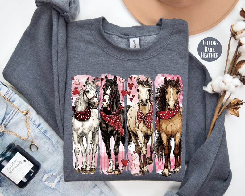 May include: Dark grey sweatshirt with a graphic of four horses wearing red bandanas and surrounded by hearts. The horses are white, black, tan, and brown. The design is on a dark grey crew neck sweatshirt.