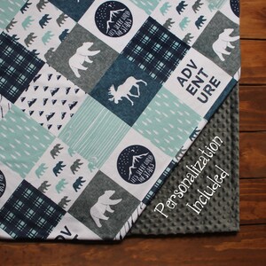 May include: A blue and gray baby blanket with a patchwork design featuring bears, moose, trees, and the text "Let's Sleep Under The Stars" and "Adventure". The blanket is made of soft, comfortable fabric and is perfect for cuddling.