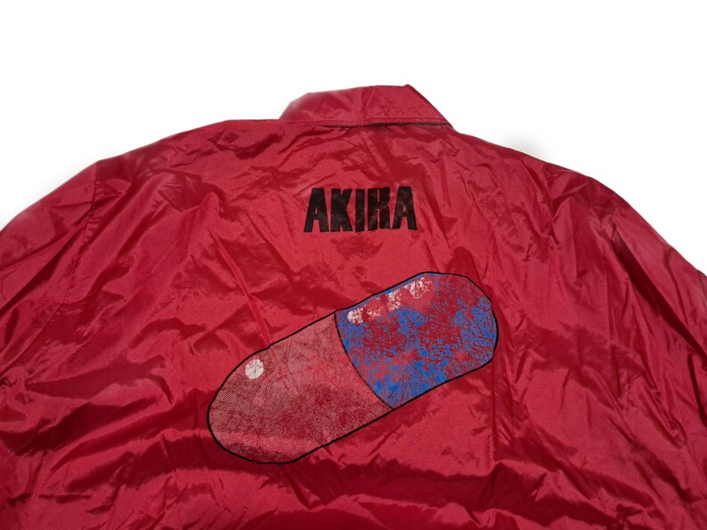 Peut inclure: Veste en nylon rouge avec un grand graphique de pilule bleu et rouge et le mot "AKIRA" imprim&eacute; au dos.