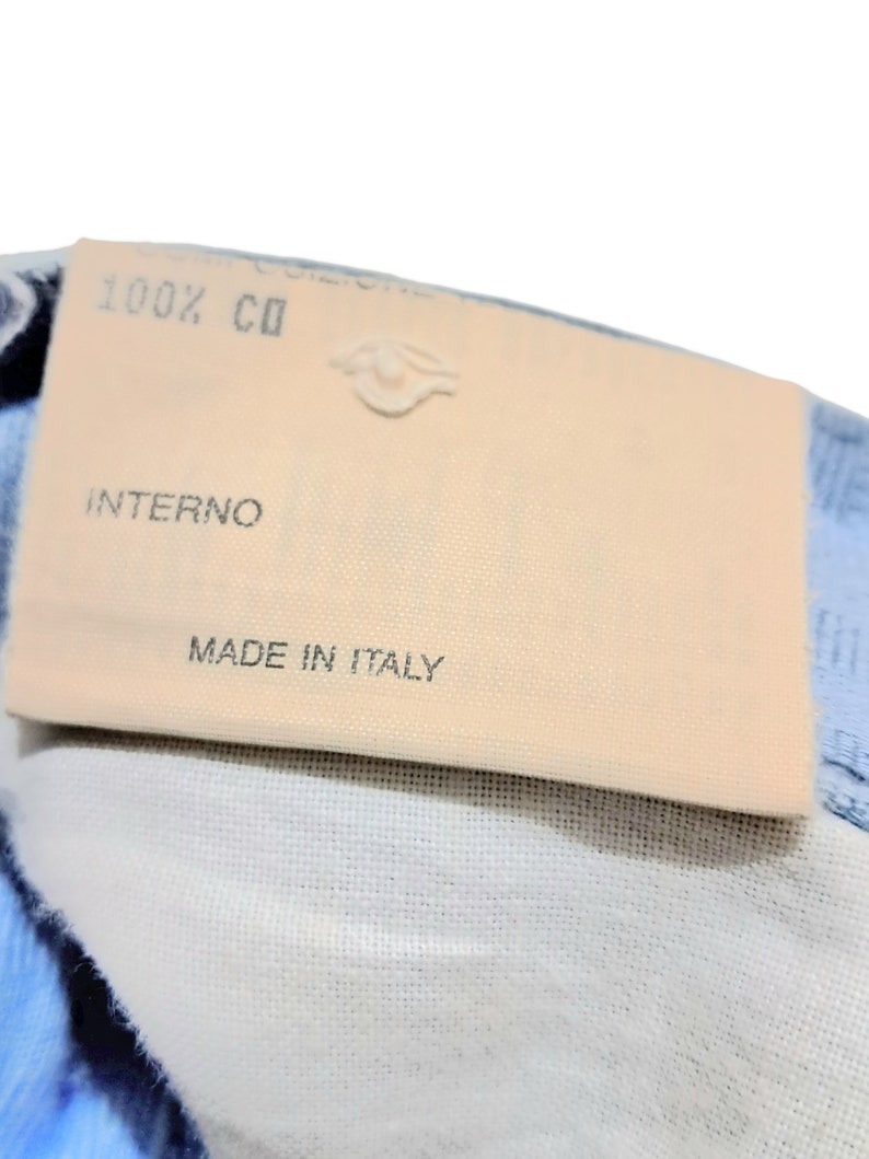 May include: A close-up of a beige fabric label with the text "100% CO", "INTERNO", and "MADE IN ITALY".