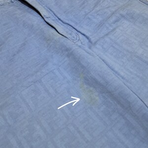 May include: Light blue pants with a subtle pattern and a small stain on the right leg. The stain is indicated by an arrow.