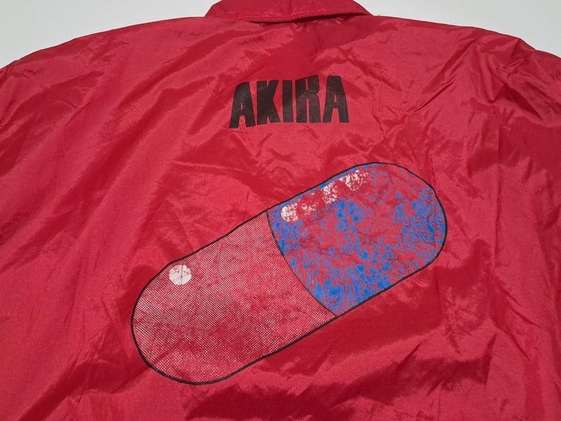 Peut inclure: Veste en nylon rouge avec un grand graphique de pilule rouge et le mot "AKIRA" imprim&eacute; en noir au dos.
