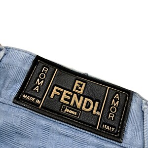 May include: A light blue pair of jeans with a black leather patch that says "FENDI Jeans" in gold lettering. The patch also has the words "Roma" and "Amor" in gold lettering. The patch also says "Made in Italy".