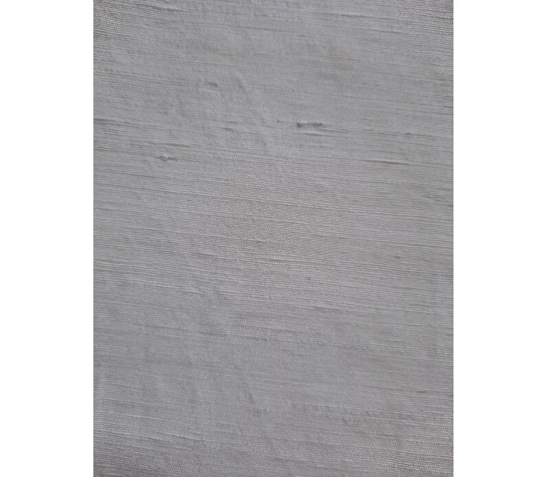 Pu&ograve; includere: Primo piano di un tessuto bianco con una sottile trama tessuta. Il tessuto ha una sensazione liscia e setosa e un leggero bagliore iridescente.