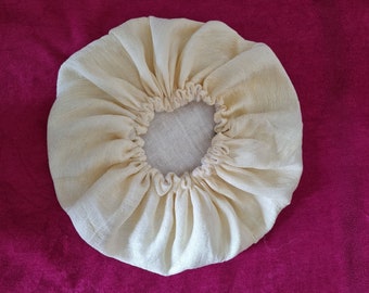 May include: A cream-colored fabric shower cap with a gathered elastic band.