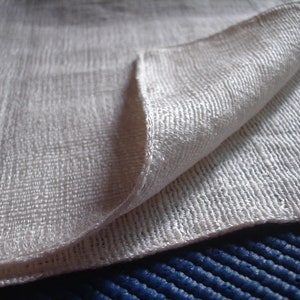 May include: A white, textured fabric folded in half. The fabric has a subtle sheen and a fine weave.