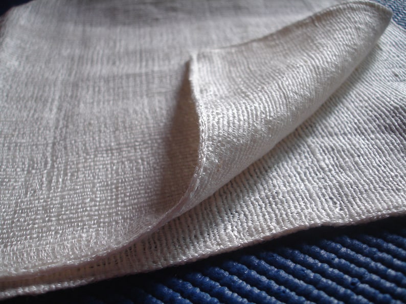May include: A white, textured fabric folded in half. The fabric has a subtle sheen and a fine weave.