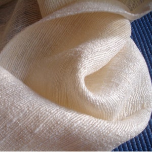 May include: A close-up of a white, textured fabric with a subtle sheen. The fabric is folded and draped, creating soft folds and curves.