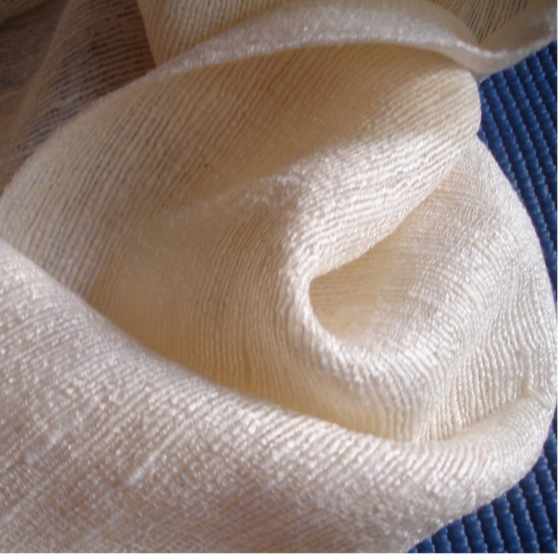 May include: A close-up of a white, textured fabric with a subtle sheen. The fabric is folded and draped, creating soft folds and curves.