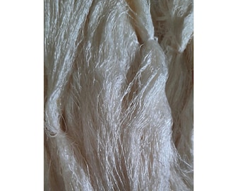 May include: Close-up of a bundle of raw, off-white silk fibers. The fibers are tightly packed and have a slightly shiny texture. The silk appears to be in its natural, unprocessed state, with a soft, delicate appearance. Ideal for textile artists and crafters.