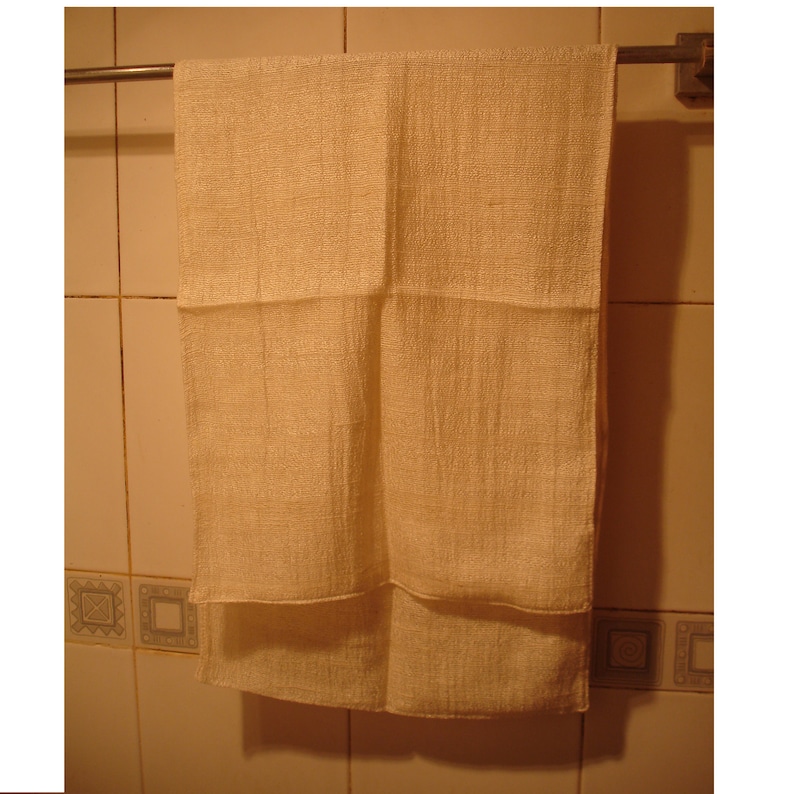 May include: A plain white hand towel hanging on a silver towel rack in a bathroom.