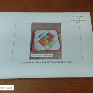 Może przedstawiać: Wz&oacute;r szycia na patchworkową matę na st&oacute;ł. Obraz przedstawia białą kopertę ze zdjęciem kolorowej pikowanej maty na st&oacute;ł. Tekst na kopercie brzmi "SEWING PATTERN FOR PATCHWORK TABLE MAT" i "Pattern Number #1042".