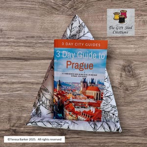 May include: A triangular fabric book holder with a black and white leaf design, displaying a "3 Day Guide to Prague" travel book. The book cover shows a Prague cityscape. The Gift Shed Creations logo is visible.