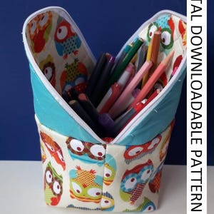 May include: A fabric pencil case with a teal top and owl pattern. The case is open, revealing colored pencils and markers. The text "DIGITAL DOWNLOADABLE PATTERN" is visible on the side.