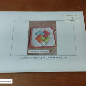 Może przedstawiać: Wz&oacute;r szycia na patchworkową matę na st&oacute;ł. Obraz przedstawia białą kopertę ze zdjęciem kolorowej pikowanej maty na st&oacute;ł. Tekst na kopercie brzmi "SEWING PATTERN FOR PATCHWORK TABLE MAT" i "Pattern Number #1042".