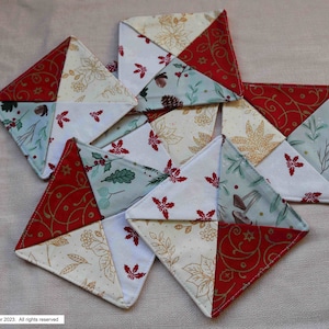 May include: Six handmade fabric coasters with a holiday theme. The coasters are made from a variety of fabrics in red, green, white, and gold. The fabric features a variety of holiday patterns, including holly, pine cones, and snowflakes.