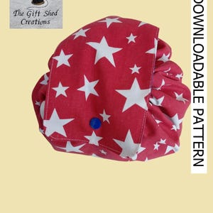 Puede incluir: Una bolsa de tela roja con un patrón de estrellas blancas, asegurada con un botón de presión azul. La imagen incluye el texto "DOWNLOADABLE PATTERN", el logotipo de The Gift Shed Creations y el aviso de derechos de autor Teresa Barker 2026.