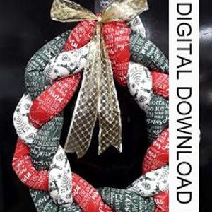 May include: A braided fabric Christmas wreath in red, white, and green with a gold ribbon and bow. The wreath is decorated with Christmas-themed text.