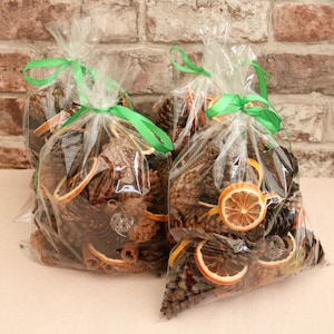 May include: Two clear plastic bags filled with dried orange slices, cinnamon sticks, and pine cones. The bags are tied with green ribbon.
