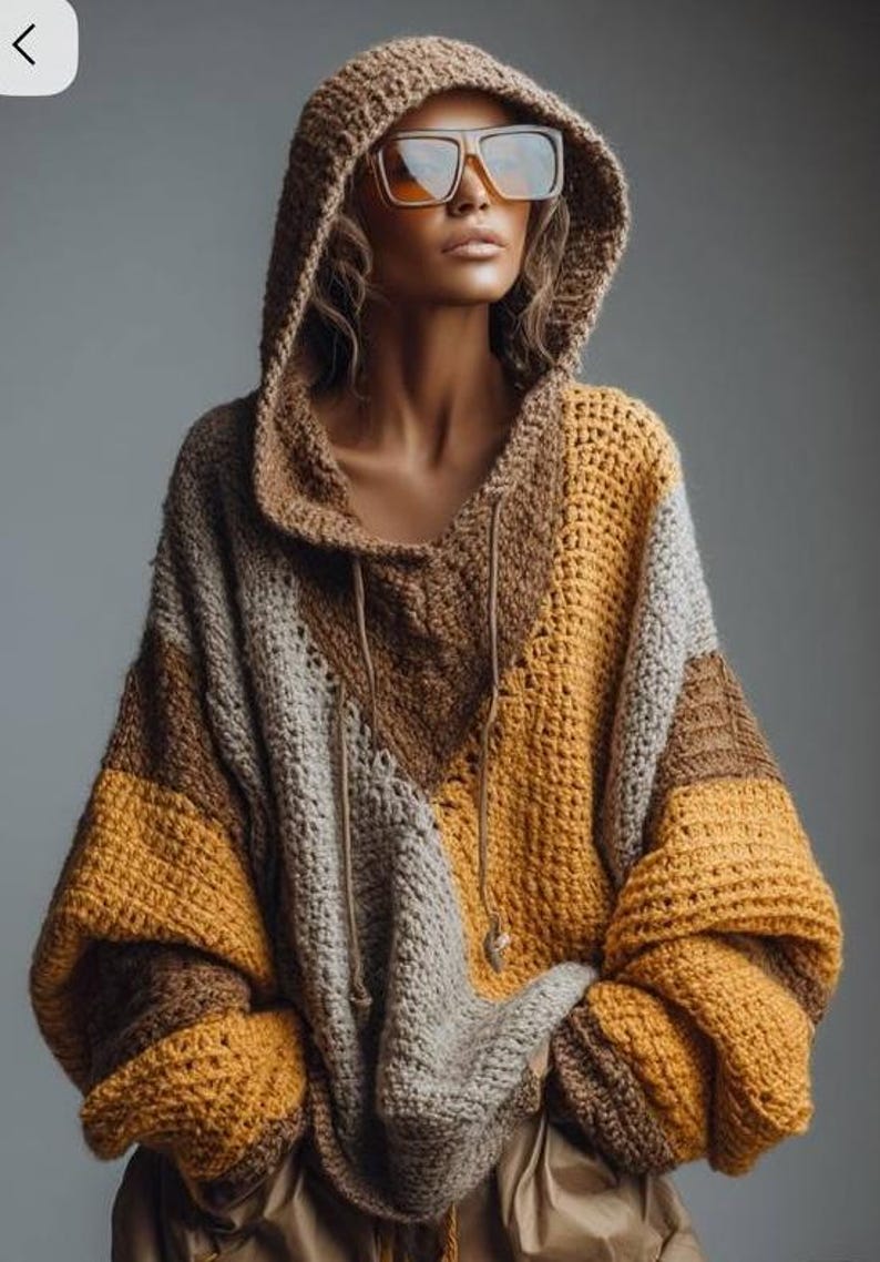 May include: A hooded crochet sweater in shades of brown, tan, and mustard yellow. The oversized sweater features a drawstring neckline and large sleeves. The model is wearing large square sunglasses.