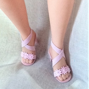 May include: A pair of lavender sandals with flower embellishments. The sandals have a criss-cross strap design and a low heel.