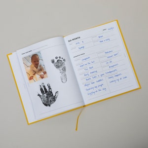 A baby handprint and a baby footprint shown in the modern baby journal to capture all the memories and milestones of the first year. A modern keepsake and lovely new baby gift or thoughtful baby shower present.