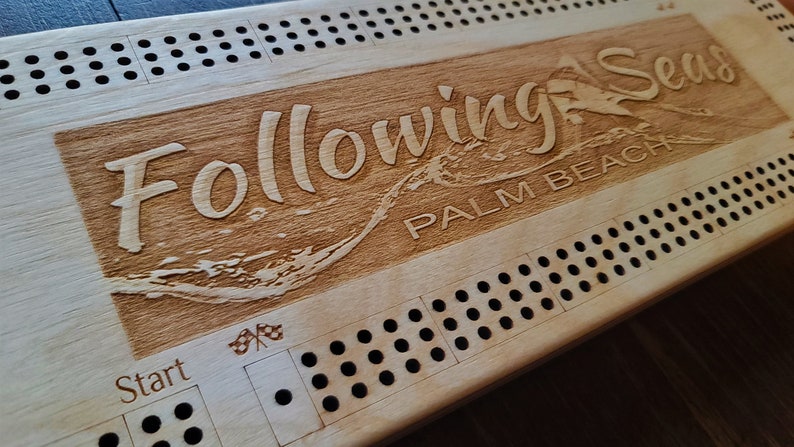 May include: A wooden game board with the words "Following Seas Palm Beach" engraved on it. The board has a grid of holes and a start space with a chequered flag.
