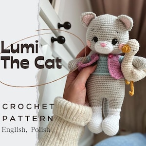Puede incluir: Muñeca Lumi The Cat de ganchillo, sosteniendo un ganso de ganchillo. El gato es gris con detalles en rosa, con un chaleco rosa y azul. El ganso es de color crema con pico y patas amarillas. Incluye el texto "CROCHET PATTERN" y "English, Polish."