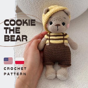 May include: A crocheted bear toy named Cookie the Bear wearing a yellow beret, a yellow and brown striped shirt, and brown overalls. The text COOKIE THE BEAR and CROCHET PATTERN is visible alongside American and Polish flag icons on the left side.