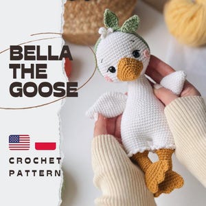 Peut inclure: Un jouet oie crocheté blanc avec un bec et des pattes orange, portant un bandeau vert avec une petite fleur blanche. Le texte BELLA THE GOOSE CROCHET PATTERN est visible sur la gauche, accompagné des drapeaux américain et polonais.