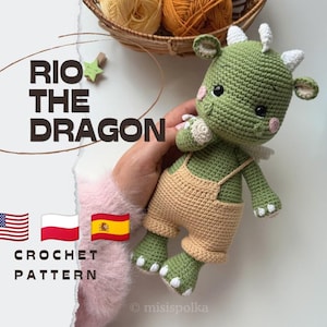 Op de afbeelding: Een groen gehaakt draakje met witte hoorns en een lichtbruine tuinbroek. De tekst RIO THE DRAGON en CROCHET PATTERN is zichtbaar, samen met Amerikaanse, Poolse en Spaanse vlagiconen. De draak heeft zwarte ogen en roze wangen.