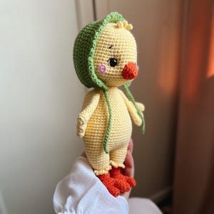 May include: A crocheted yellow chick toy with a green crocheted hat. The chick has orange feet and a pink nose.