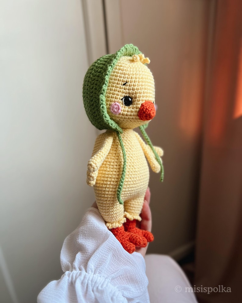 May include: A crocheted yellow chick toy with a green crocheted hat. The chick has orange feet and a pink nose.