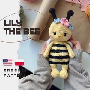 Pode incluir: Uma boneca abelha de crochê chamada Lily the Bee com um corpo listrado de amarelo e preto, antenas pretas e uma coroa de pequenas flores azuis e rosas. A boneca tem olhos bordados e bochechas rosas. O texto LILY THE BEE CROCHET PATTERN é visível.