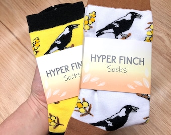 May include: Two pairs of socks featuring a black and white magpie design. The socks are yellow and white with a brown cuff. The socks have a tag that says "HYPER FINCH Socks".