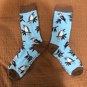 May include: A pair of blue socks with a brown and white kookaburra bird pattern. The socks have the text "Under Finch" on the side.