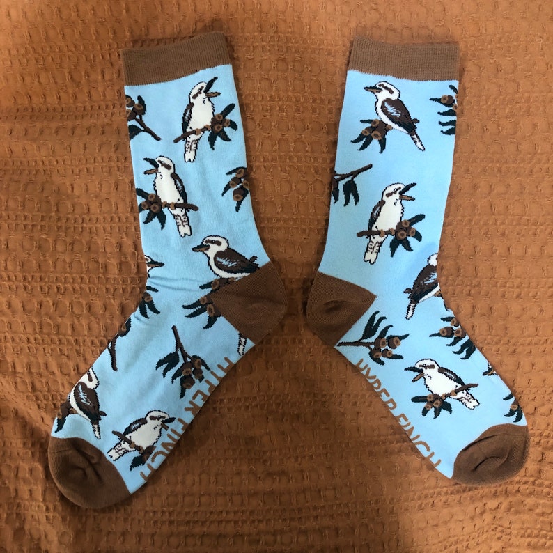 May include: A pair of blue socks with a brown and white kookaburra bird pattern. The socks have the text "Under Finch" on the side.