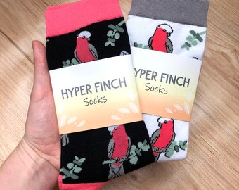 May include: Two pairs of socks with a black and white bird pattern. The socks have a pink and gray cuff. The socks have a label that says "Hyper Finch Socks".