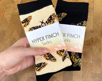 May include: Two pairs of socks with a moth pattern. One pair is beige with black accents and the other is black with beige accents. The socks have a black cuff and toe. The packaging reads "HYPER FINCH Socks".