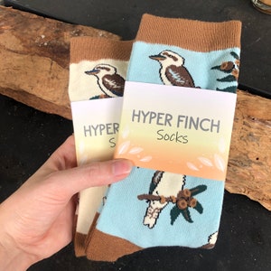 May include: Two pairs of socks with a brown cuff and a blue background. The socks feature a cartoon image of a kookaburra bird. The socks are packaged with a tag that reads "HYPER FINCH Socks".