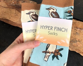 May include: Two pairs of socks with a brown cuff and a blue background. The socks feature a cartoon image of a kookaburra bird. The socks are packaged with a tag that reads "HYPER FINCH Socks".