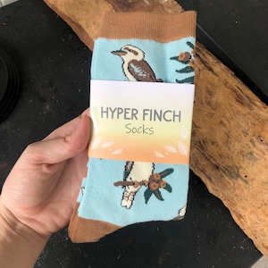 May include: A pair of blue socks with a brown cuff. The socks feature a white bird with brown markings and a green leafy branch with brown berries. The socks have a white tag that reads "HYPER FINCH Socks".