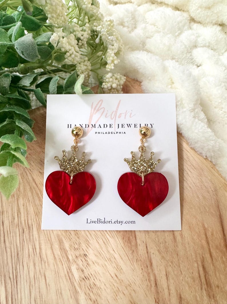 Pode incluir: Brincos em forma de cora&ccedil;&atilde;o vermelho com coroas douradas com glitter. Os brincos est&atilde;o em um cart&atilde;o branco com o texto "Bidori Handmade Jewelry Philadelphia" e "LiveBidori.etsy.com".