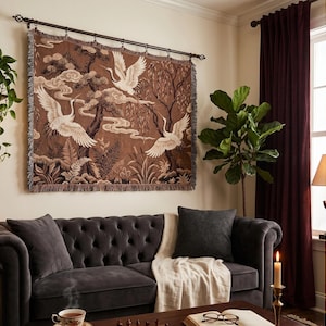 May include: A rectangular woven wall tapestry featuring a brown background with three white cranes in flight, stylized trees, and clouds. The tapestry has a fringed bottom edge and is suspended from a dark metal rod with decorative finials.