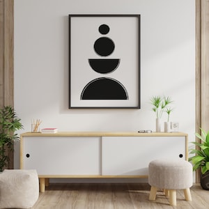 May include: A black and white abstract geometric print in a black frame hanging on a white wall above a light wood cabinet with white doors. The cabinet is sitting on a wood floor. There is a small stool in front of the cabinet.