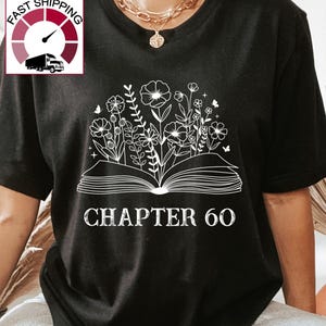 May include: Black t-shirt with a white design of an open book with flowers growing out of it. The text "CHAPTER 60" is below the book.