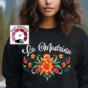 May include: Black sweatshirt with the text "La Madrina" in white cursive lettering and a colorful floral design below.
