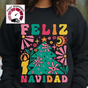 May include: A black sweatshirt with a colorful graphic design featuring the words "Feliz Navidad" and a stylized Christmas tree with flowers, stars, and a candle.
