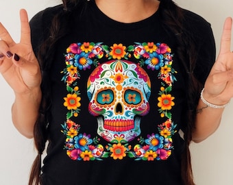 May include: Black t-shirt with a colorful sugar skull design surrounded by flowers. The skull has blue eyes, a pink nose, and a white and pink mouth.